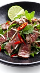 Colorful spicy beef salad with cilantro, mint, and lime, beautifully arranged on a black stone plate, bright and airy composition.
