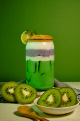 Fresh kiwi and taro layered drink in a glass jar with lime slice and mint leaves, served on green background.