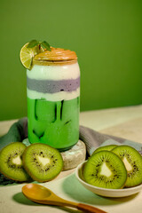 Kiwi smoothie and taro milk blend in glass jar, cold drink concept with artistic green backdrop.
