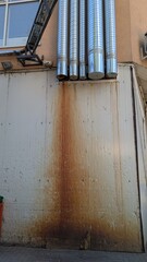 An aged and rusty industrial wall that features numerous metal pipes and various textures