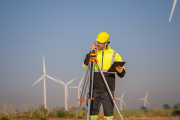 Engineer working in front of wind turbines for checking wind turbines of the field during beautiful sunset. Alternative energy concept.