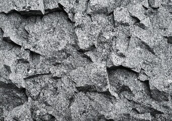 Close-up view of rough textured gray stone wall with irregular fragmented rock surfaces and sharp edges