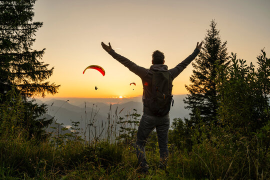 Hiker with backpack enjoying sunset view and paragliders in the mountains