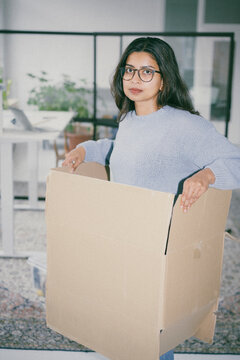 Woman standing in loft office looking uncertain inside a cardboard box