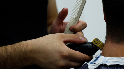 A barber is using an electric clipper and a comb to cut a client's hair