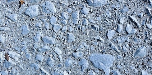 A rough surface of gravel and concrete emerges under direct light, highlighting textures and contrasts. This banner evokes raw materiality, the memory of ground, and the beauty of unseen details. 