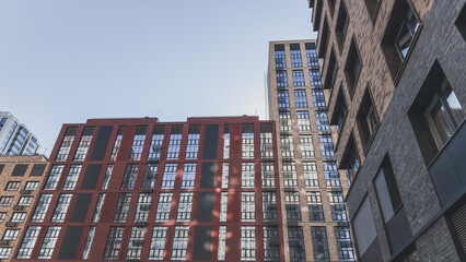Fototapeta premium Modern residential buildings with glass windows and brick facades against a clear blue sky, representing contemporary urban architecture, city development, and modern housing design