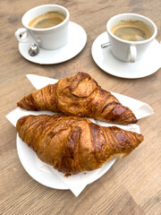 buttery croissants and espresso coffee cups on wooden table in cafe, morning breakfast