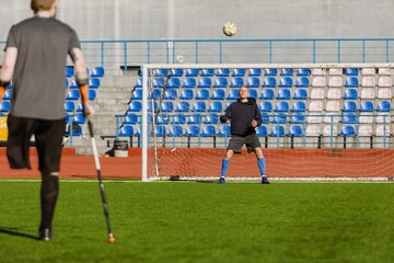 A man on crutches stands and watches as another man on goal is about to catch the ball