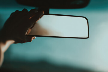 Hand adjusting rearview mirror inside car close up minimal style soft natural light focus on reflection transportation safety modern vehicle interior calm mood
