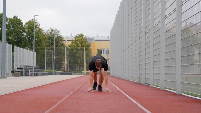 Frontal view of young white male athlete placing hands down preparing to sprint on track