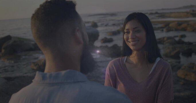 Standing couple facing each other on rocky beach at sunset, with tide pools and ocean water - Powered by Adobe