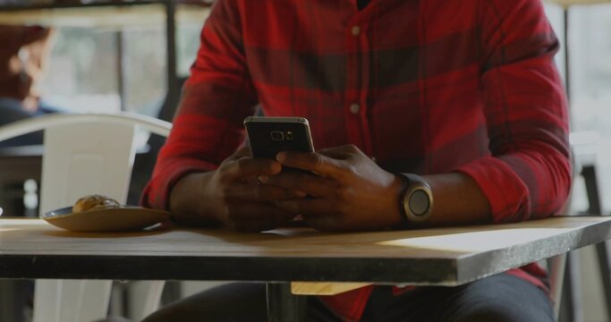 Man wearing red plaid shirt and smartwatch scrolling smartphone screen in cafe, with pastry plate - Powered by Adobe