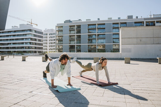 Male and female athletes lift their legs while standing in push-up position on mats - Powered by Adobe