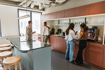 Two female workers are looking at a phone that one of them is holding while two men are standing next to them drinking from cups