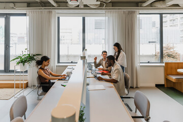 Obraz premium A group of three workers are sitting at a table while one of them is talking to a female worker standing next to him