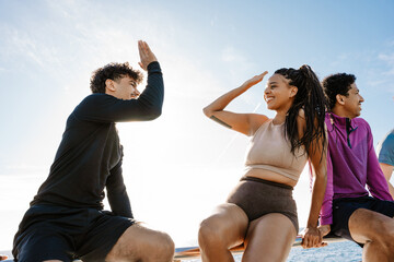 Male and female athletes sitting on a fence and giving each other a high five while smiling