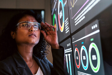 Professional with smart glasses examines interactive data dashboards on large screens, focusing on colorful analytics and digital metrics in a high tech workspace.