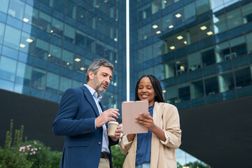 Diverse business colleagues discussing while watching tablet outdoors