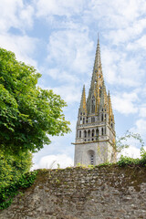 The Gothic spire of the church in Pont-Croix, Brittany, a region of France, rises above a peaceful garden path and a stone wall.