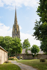The Gothic spire of the church in Pont-Croix, Brittany, a region of France, rises above a peaceful garden path and a stone wall.