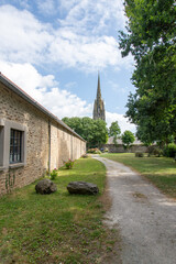 The Gothic spire of the church in Pont-Croix, Brittany, a region of France, rises above a peaceful garden path and a stone wall.