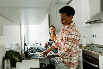A man washes his fork while a woman stands next to him wiping her plate