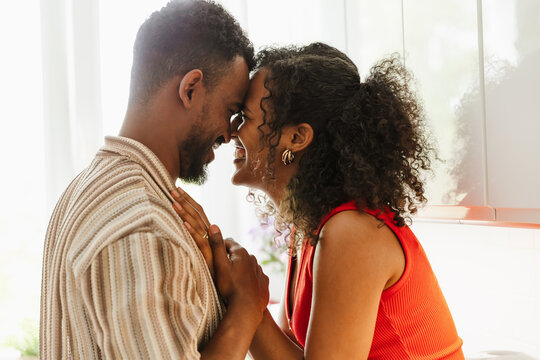 A man and a woman touch their foreheads and smile while she puts her hand on his chest