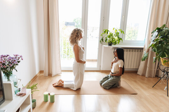 A mother kneels on a mat opposite her daughter who sits across from her