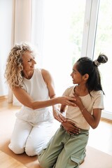 Fototapeta premium A mother helps her daughter place her hands while they smile and sit on the mat