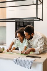 A father stands at the table and helps his daughter roll out dough