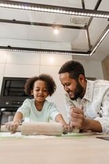A father leans on the table and smiles as he watches his daughter roll out dough