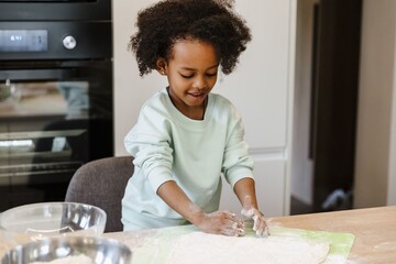 The daughter smiles and holds her hands near the dough while standing at the table