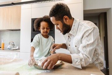 Father and daughter put the dough in a baking dish while standing at the table