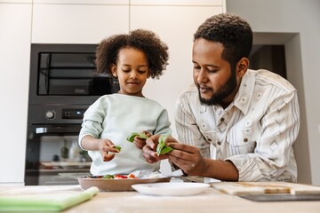 A father and his daughter stand at a table and hold greens
