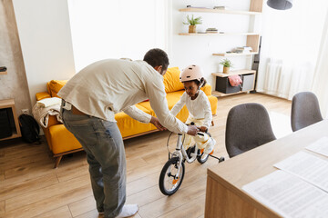 A father supports the bicycle on which his daughter rides