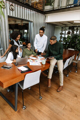 A group of five workers are talking while two of them are sitting at a table and three of them are standing