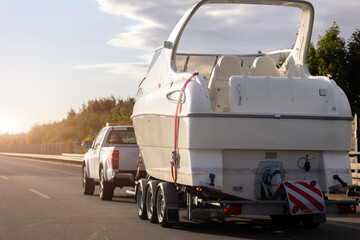 Big luxury cabin motorboat cruiser yacht trailer pick-up SUV carrier river lake highway road sunset summer light. Luxury rich fishing leisure recreation lifestyle. Service maintenance transportation