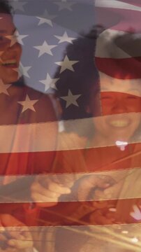 Animation of national flag of america over diverse friends with sparklers enjoying at beach