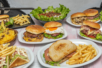 Still life with a variety of burger sliders, potato wedges, and creative sauces on a large wooden board