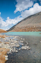 Shoreline of lake Akchan, glacial lake located in the Altai mountains, with cloudy blue sky above, Russia