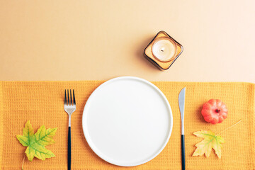 White plate with cutlery, autumn leaves and candle on yellow napkin. Flat lay table setting with copy space, mockup