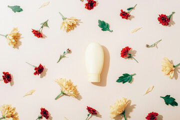 Yellow cosmetic bottle with yellow and red chrysanthemums on beige background. Flat lay natural beauty composition. Top view, mockup