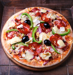 Pizza with chorizo ​​sausage, mozzarella cheese, and black olives. Rustic wooden background. Soft focus.	