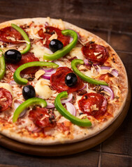 Pizza with chorizo ​​sausage, mozzarella cheese, green pepper and black olives. Rustic wooden background. Soft focus.	