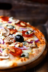 Pizza with chorizo ​​sausage, mozzarella cheese, and black olives. Rustic wooden background. Soft focus.	