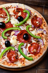 Pizza with chorizo ​​sausage, mozzarella cheese, green pepper and black olives. Rustic wooden background. Soft focus.	