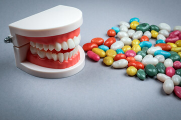 Dental model with artificial teeth next to colorful candies on gray background symbolizing sugar consumption and oral health care awareness concept