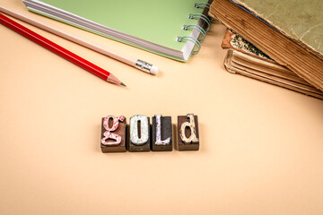 Word gold made from vintage wooden letterpress blocks with pencils and old books on beige background symbolizing wealth value and success concept