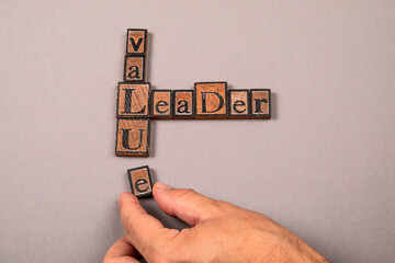 Words leader and value made from vintage wooden letterpress blocks with human hand arranging letters on gray background symbolizing leadership integrity and business ethics